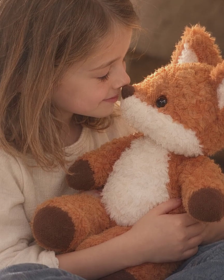 Rovan the fox plush shared with a child in a softly lit linen play fort.